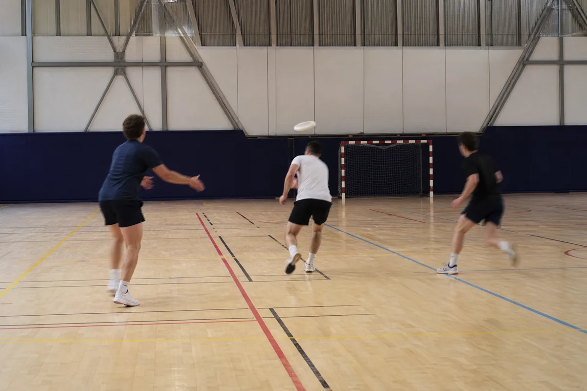 Séance d’entraînement de frisbee en salle, joueurs en mouvement sur un parquet de gymnase, éclairage artificiel