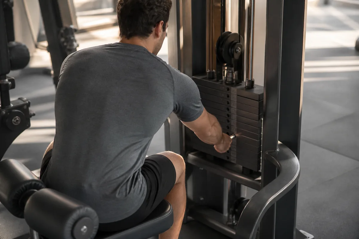 Personne vue de dos ajustant la charge d&rsquo;une machine de musculation, mains sur la goupille métallique
