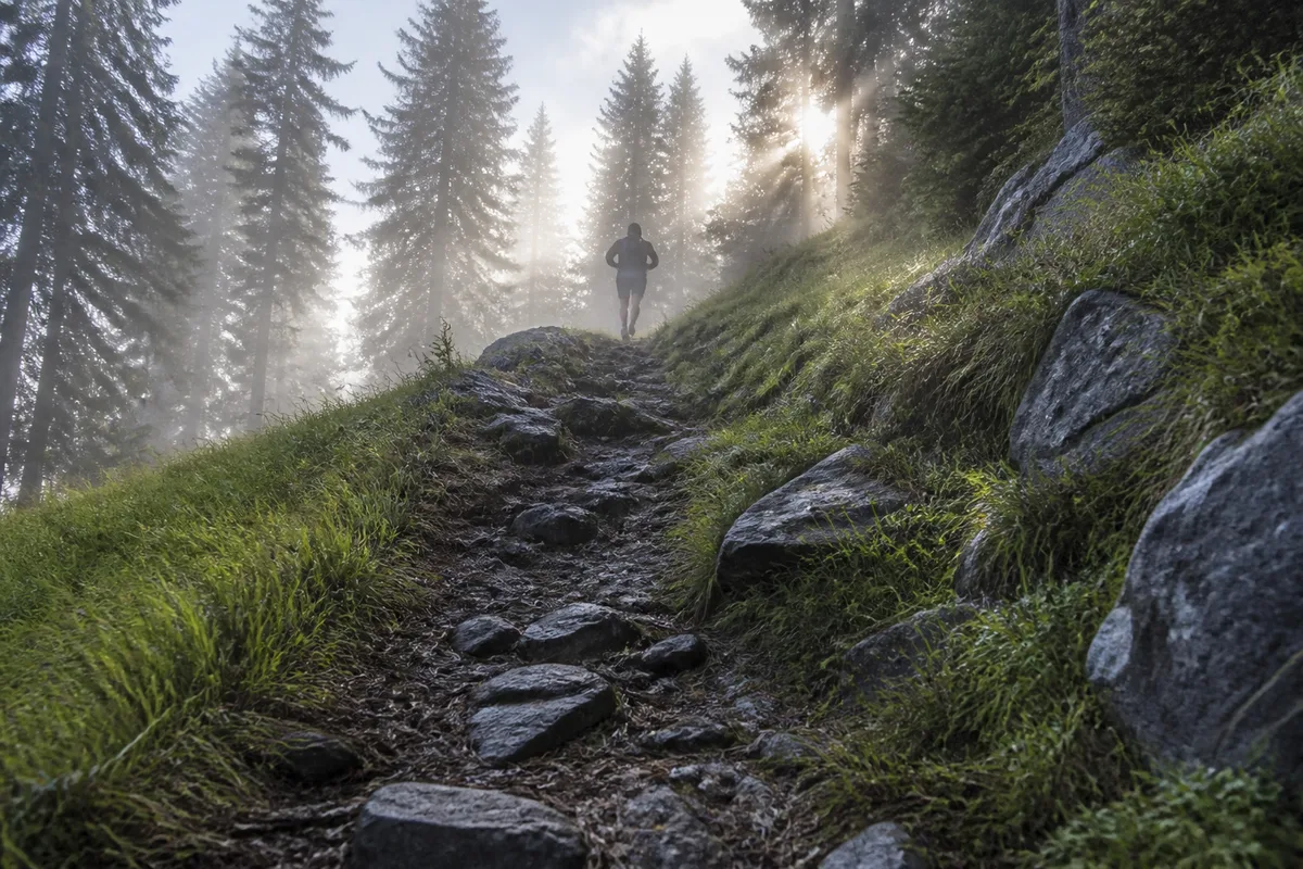 Coureur de dos gravissant un sentier de montagne dans la brume matinale
