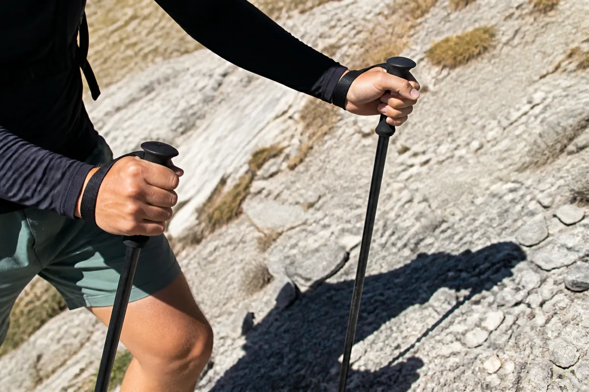 Bâtons de trail et mains en appui sur un sentier caillouteux en forte pente