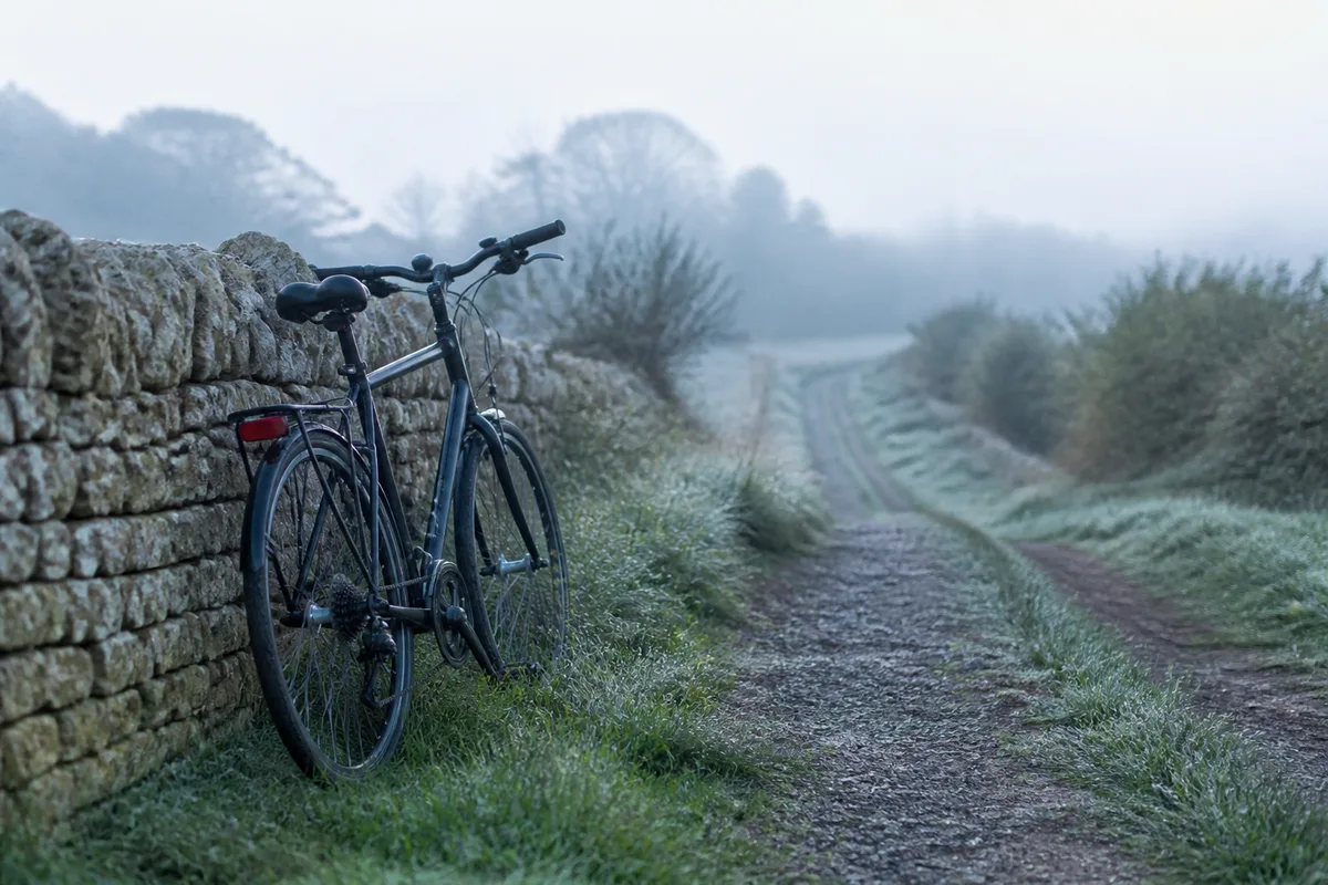 Vélo appuyé contre un muret au bord d&rsquo;un chemin de campagne au petit matin, brume légère